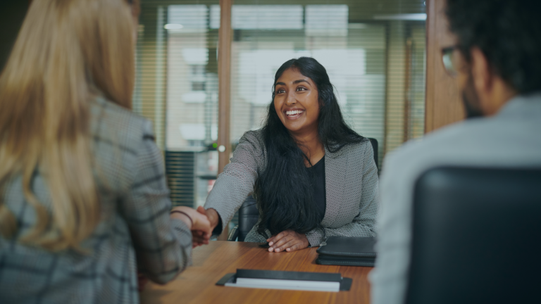 Constructive feedback to candidates: young graduate keen to impress at her first interview shaking hands with the female interviewer, man sitting beside the interviewer can only see the back of their heads